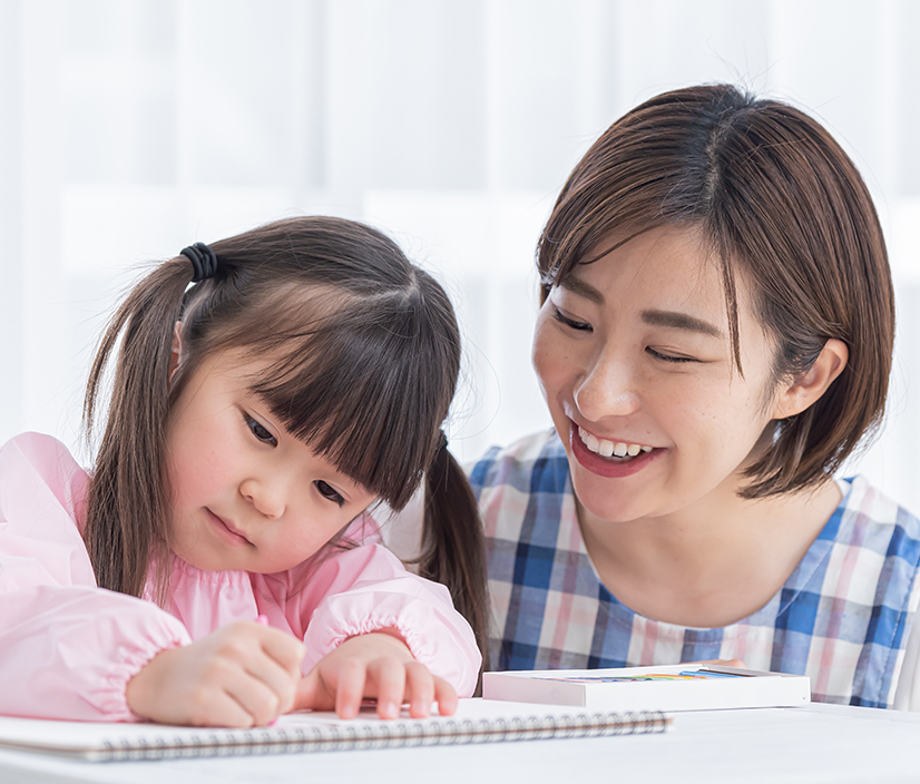 女の子がお絵描きをする様子を見守る保育士